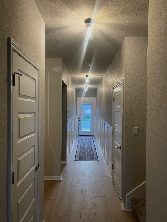 Hallway featuring a textured wall, light wood-style flooring, a decorative wall