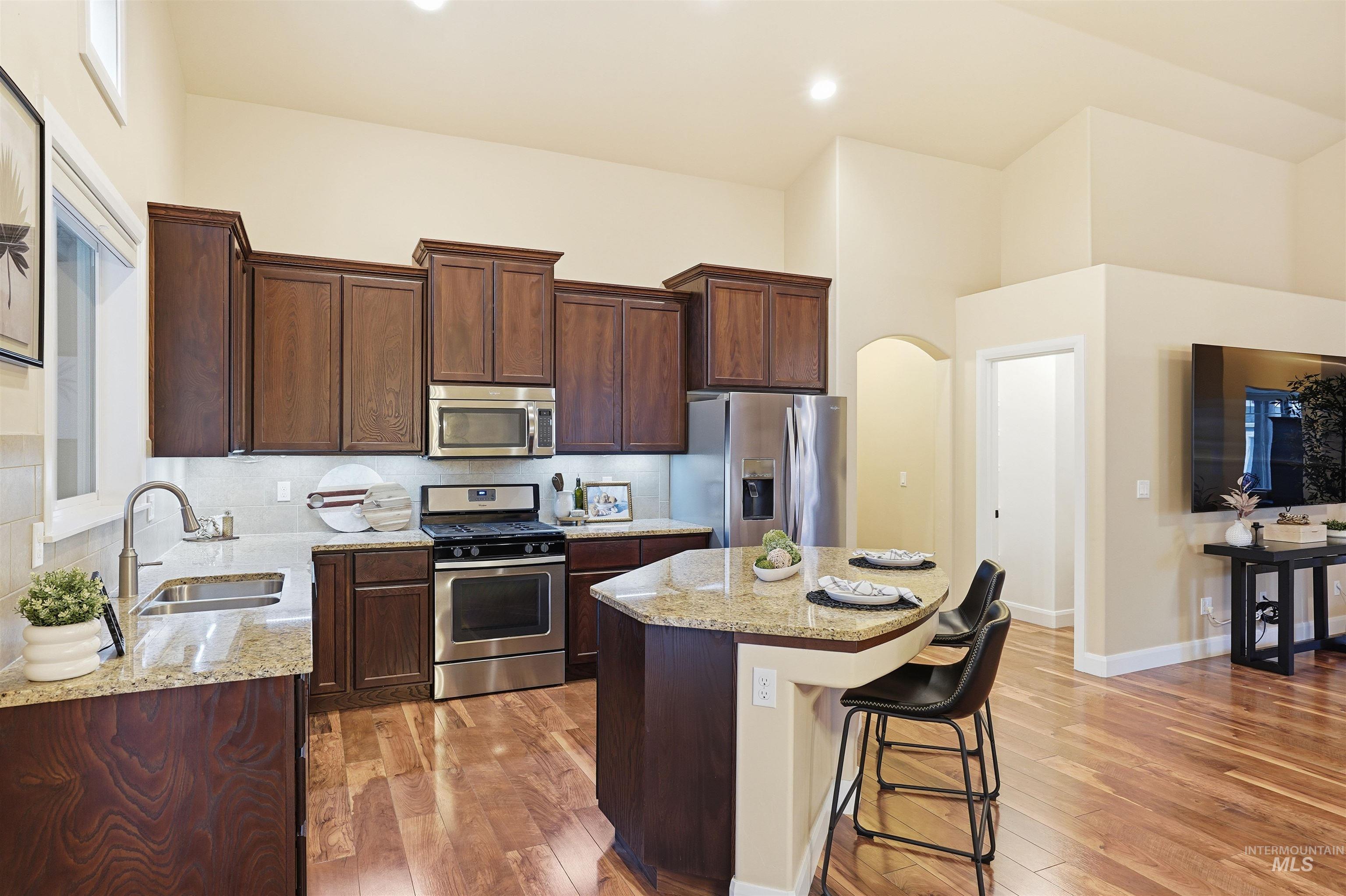 5697 Combermere Drive Eagle, ID 83616 - Photo 11 of 43 Kitchen with light stone countertops, appliances with stainless steel finishes, arched walkways, a center island, and a towering ceiling