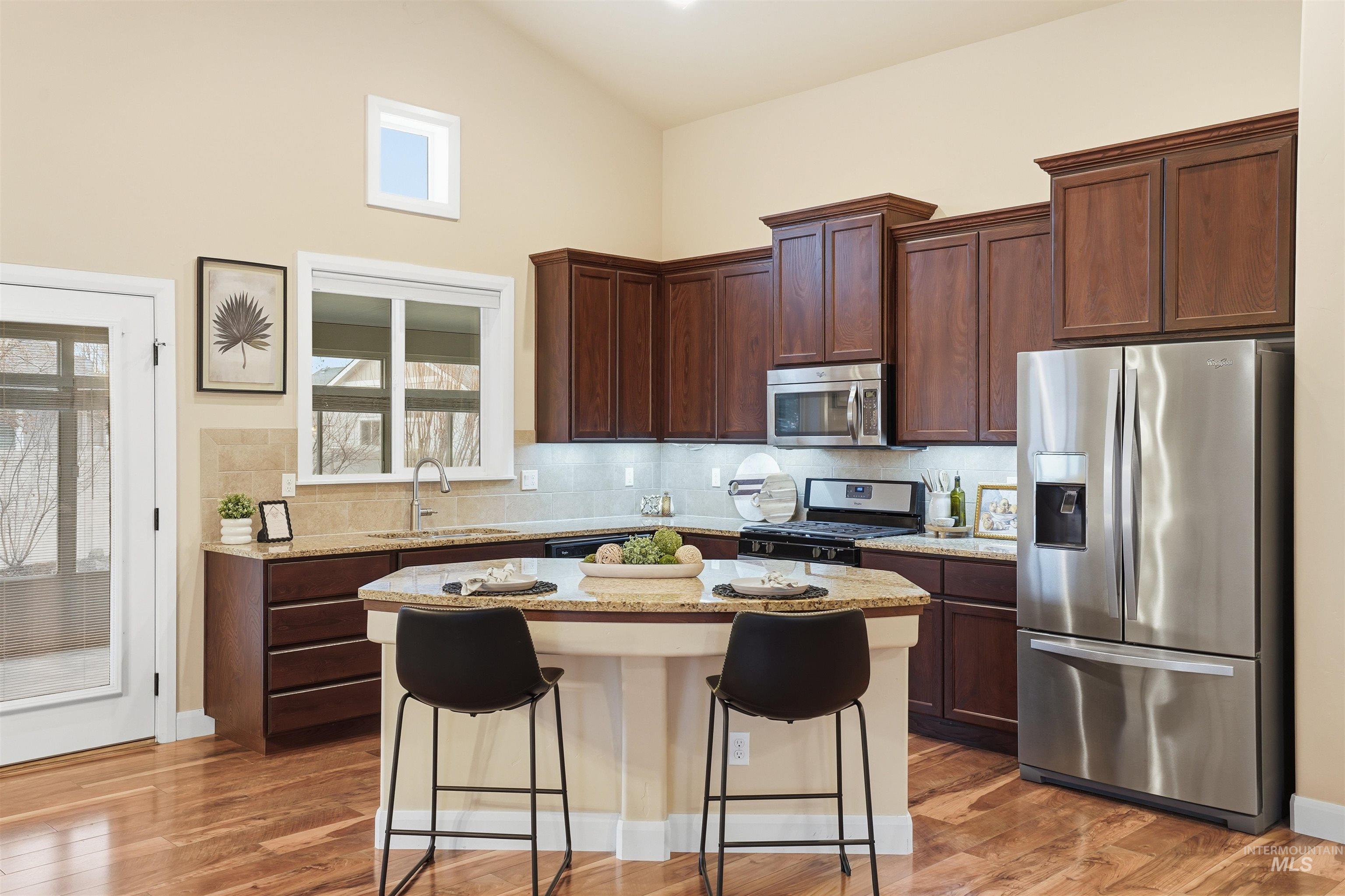 5697 Combermere Drive Eagle, ID 83616 - Photo 9 of 43 Kitchen featuring stainless steel appliances, light stone countertops, a breakfast bar, a center island, and tasteful backsplash