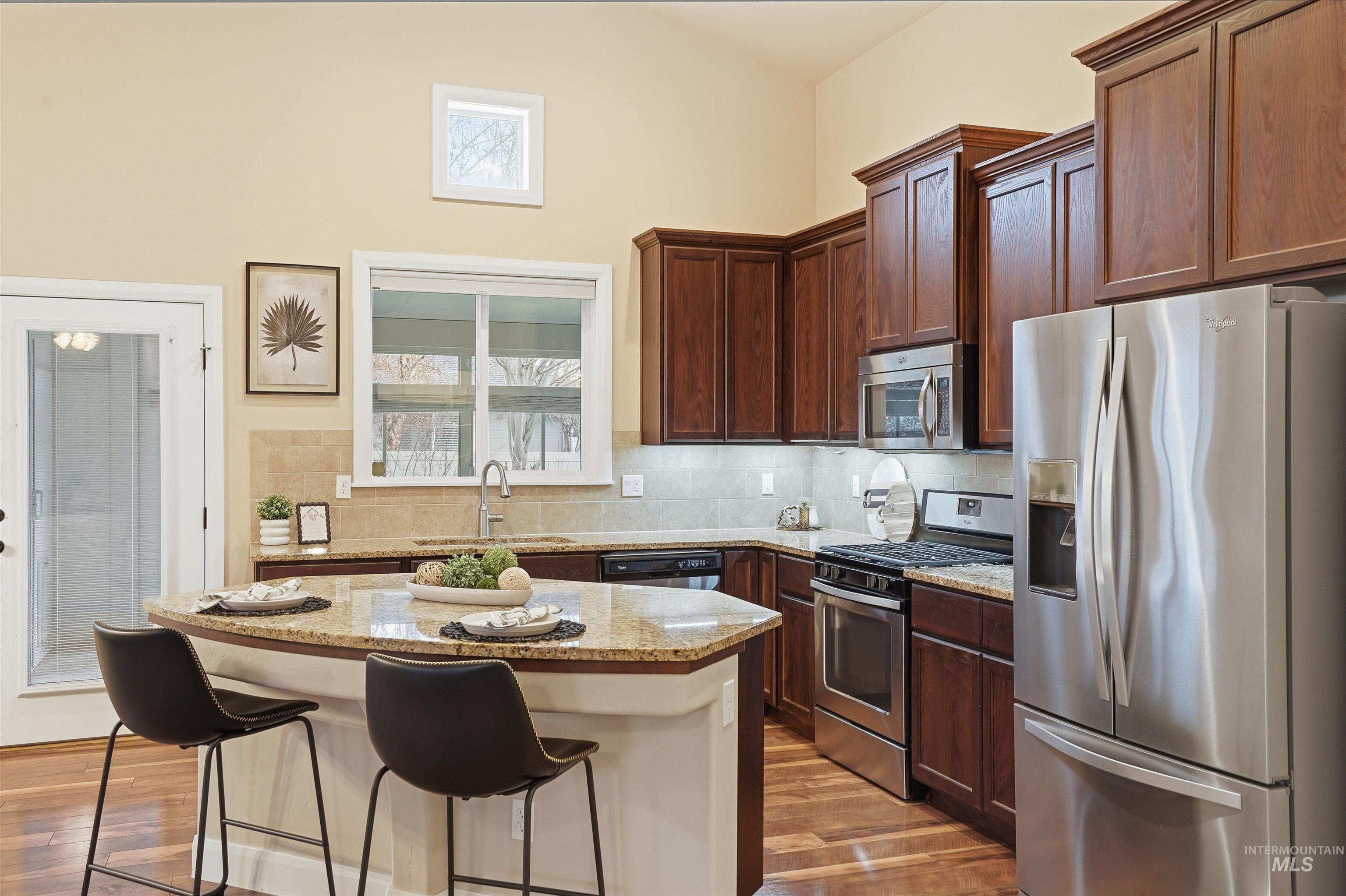 5697 Combermere Drive Eagle, ID 83616 - Photo 10 of 43 Kitchen featuring stainless steel appliances, a kitchen breakfast bar, light stone countertops, backsplash, and high vaulted ceiling