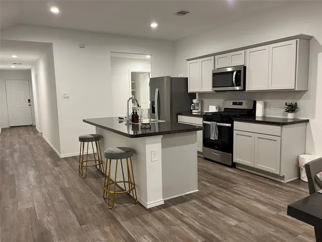 a kitchen with stainless steel appliances granite countertop a stove top oven a sink dishwasher a refrigerator and white cabinets with wooden floor