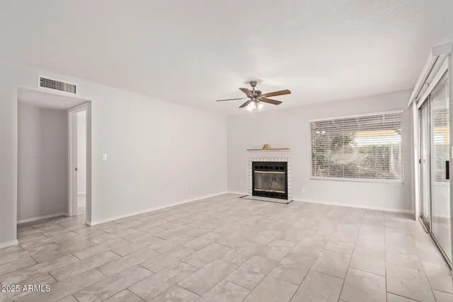 a view of an empty room with chandelier fan and fire place