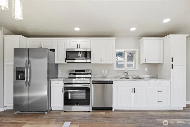 a kitchen with stainless steel appliances granite countertop a refrigerator a stove a sink and white cabinets with wooden floor