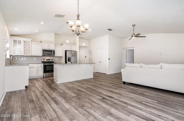 a large white kitchen with kitchen island a stove a sink dishwasher and a refrigerator with wooden floor