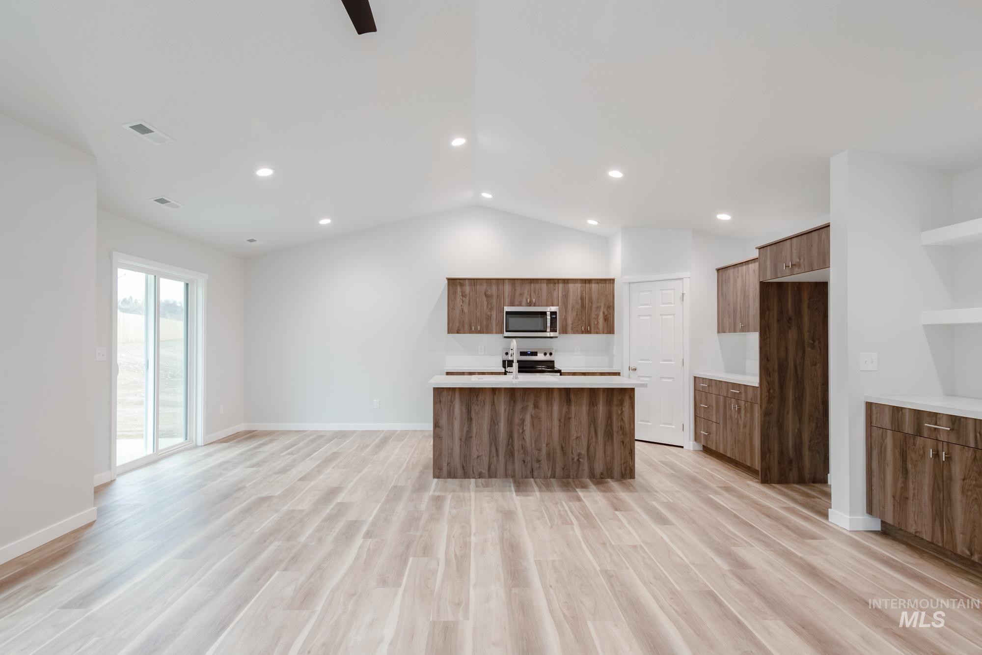 1576 Long Pond Street Middleton, ID 83644 - Photo 22 of 22 Kitchen featuring a center island with sink, light wood-style floors, open floor plan, lofted ceiling, and brown cabinetry