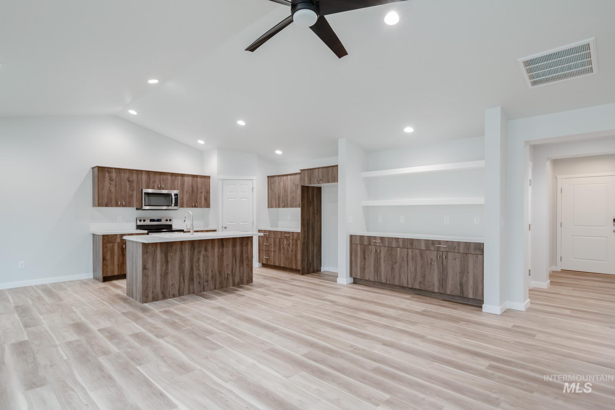 1576 Long Pond Street Middleton, ID 83644 - Photo 12 of 22 Kitchen featuring a center island with sink, light wood-style floors, a ceiling fan, appliances with stainless steel finishes, and brown cabinetry