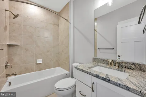 a bathroom with a granite countertop bathtub shower sink vanity mirror and toilet