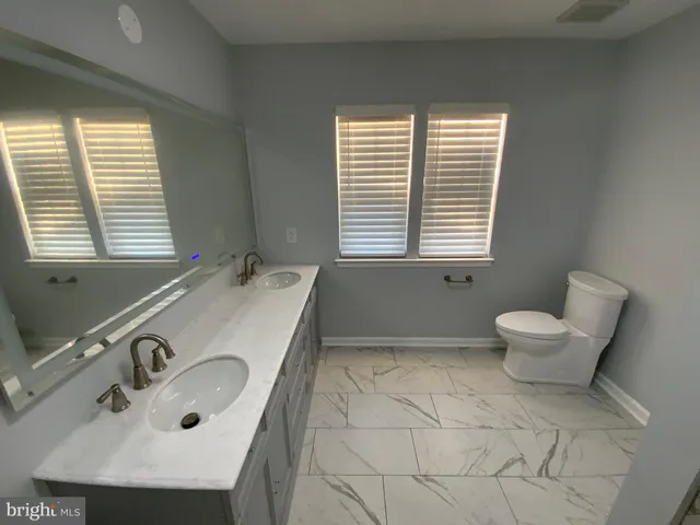 a bathroom with a granite countertop sink a toilet and a window