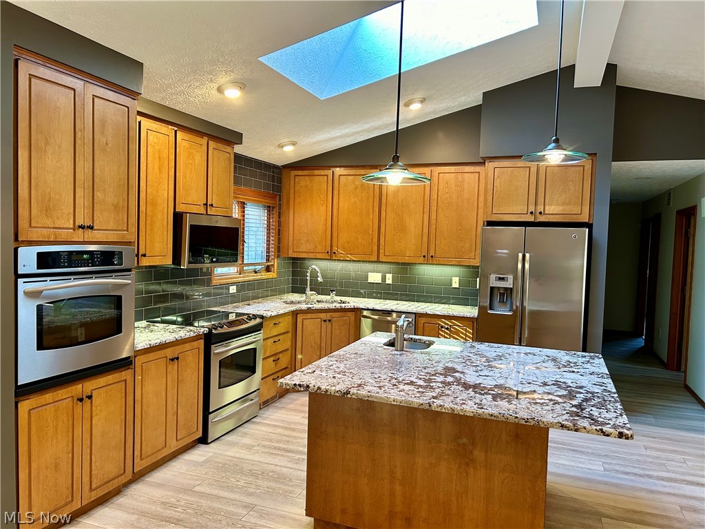 8763 Timber Edge Drive North Ridgeville, OH 44039 - Photo 7 of 40 Kitchen featuring light hardwood / wood-style flooring, appliances with stainless steel finishes, an island with sink, decorative light fixtures, and vaulted ceiling with skylight