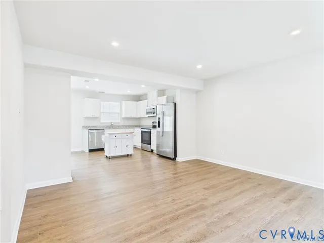 a view of an empty room with wooden floor and a kitchen