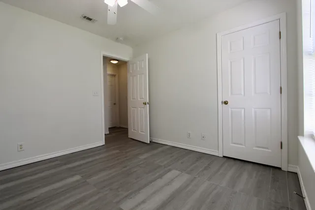 an empty room with wooden floor closet and windows