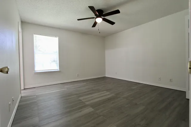 an empty room with wooden floor ceiling fan and windows