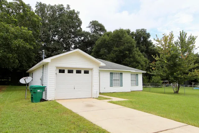a view of a white house with a yard and large trees with wooden fence
