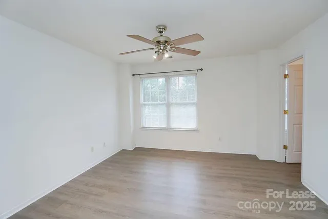 an empty room with wooden floor chandelier fan and windows