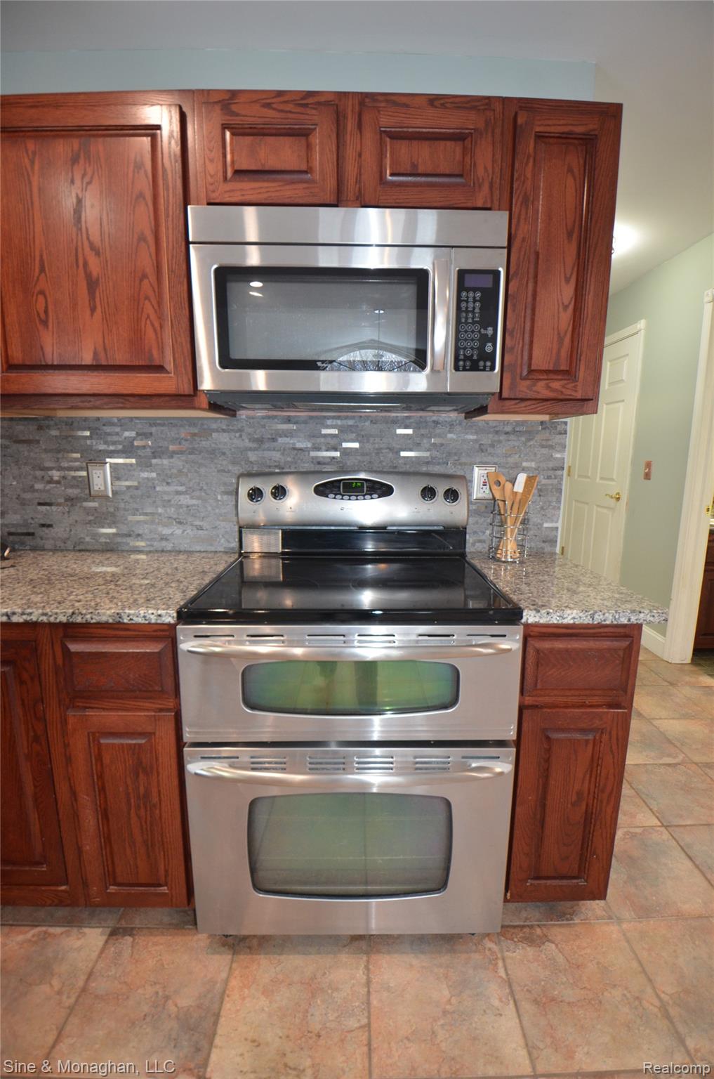76152 Burman Road Richmond, MI 48062 - Photo 19 of 75 Kitchen with appliances with stainless steel finishes, decorative backsplash, light stone counters, and brown cabinets