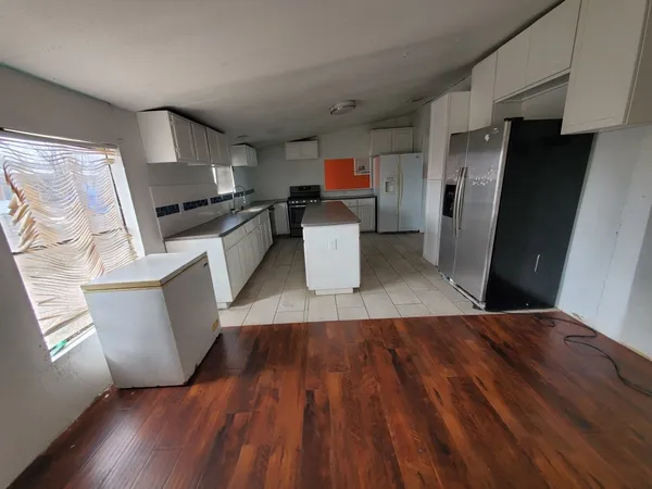 a living room with stainless steel appliances furniture a refrigerator a sink a microwave a stove and white cabinets