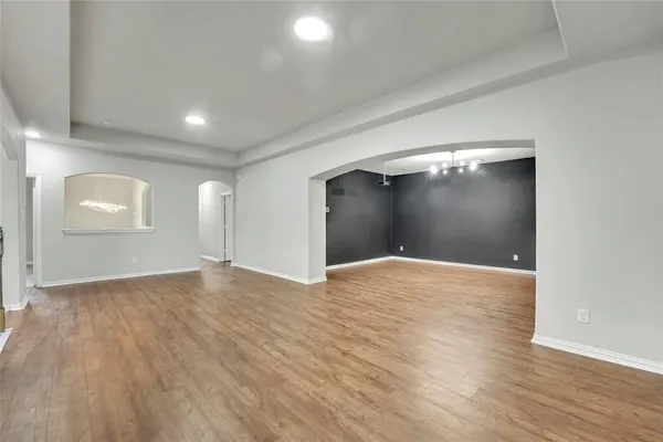 a view of an empty room with chandelier and wooden floor