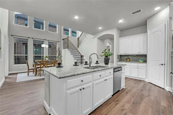 a kitchen with stainless steel appliances granite countertop a refrigerator a stove top oven a sink dishwasher and white cabinets with wooden floor