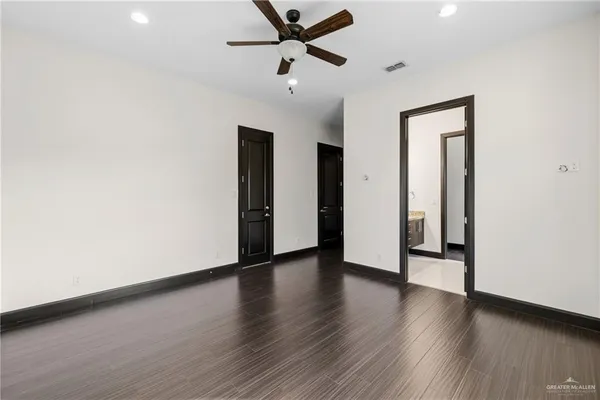 a view of an empty room with wooden floor and a ceiling fan