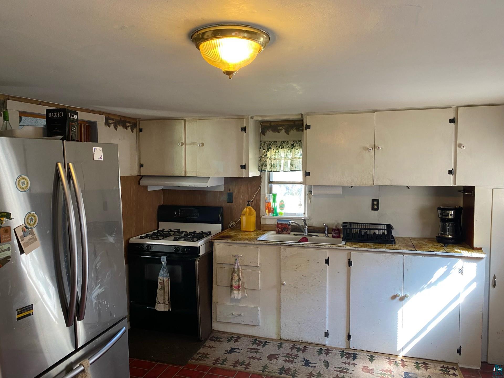 W6402 Old Bass Lake Road Minong, WI 54859 - Photo 5 of 18 Kitchen with range hood, white gas range, stainless steel refrigerator, sink, and dark tile patterned floors