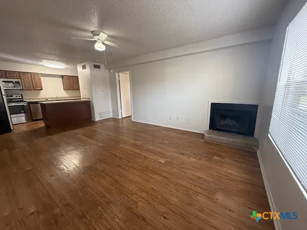 an empty room with wooden floor kitchen view and windows