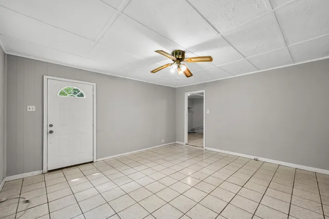 an empty room with chandelier fan and windows