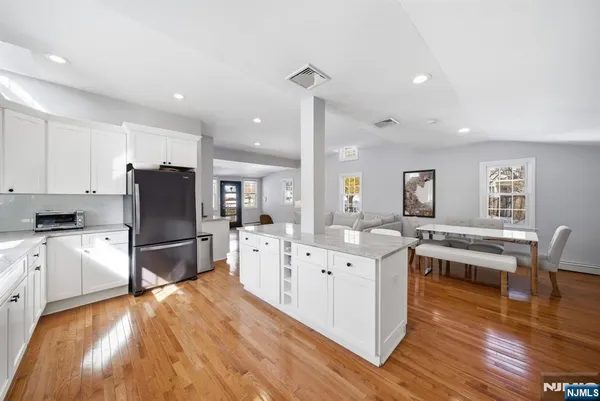 a kitchen with stainless steel appliances kitchen island granite countertop a refrigerator a stove a sink a dining table and chairs with wooden floor