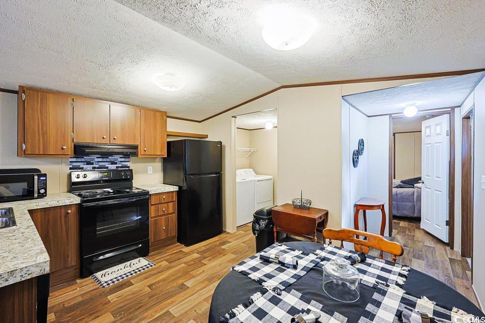 255 Quail Run Road Loris, SC 29569 - Photo 5 of 29 Kitchen with black appliances, light countertops, a textured ceiling, light wood-style floors, and brown cabinetry
