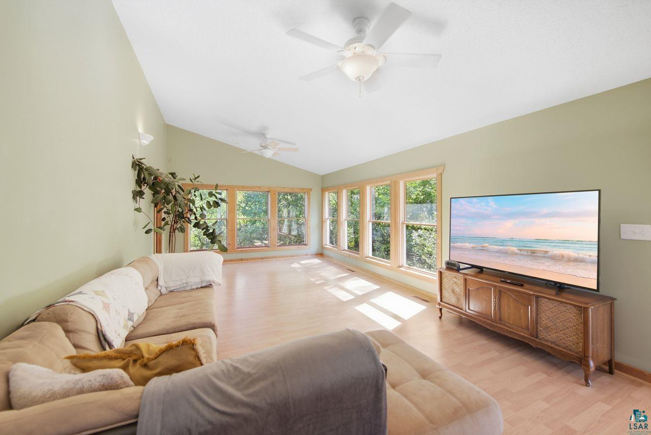 65889 Old County Road Marengo, WI 54855 - Photo 4 of 44 Vaulted ceiling with ceiling fans, a wall of windows with wood trim, light wood-finish flooring, and wall-mounted sconce lighting