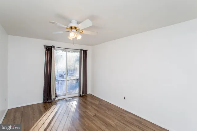 an empty room with wooden floor fan and windows