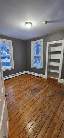 an empty room with wooden floor closet and windows