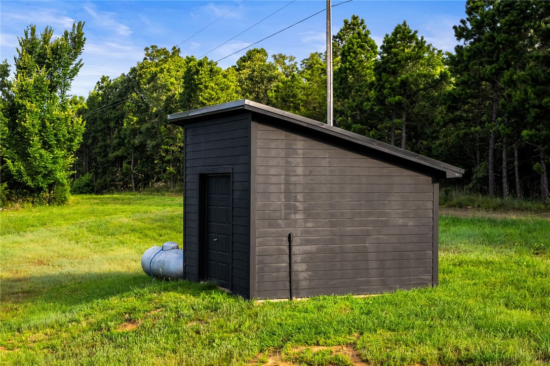 11334 Pool Holw Road Dardanelle, AR 72834 - Photo 32 of 50 Modern black shed with a single entry door and a sloped roofline, set within a grassy expanse