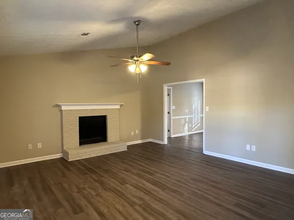 a view of an empty room with wooden floor fireplace and a window