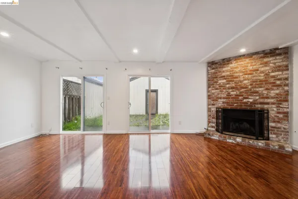 an empty room with wooden floor fireplace and windows