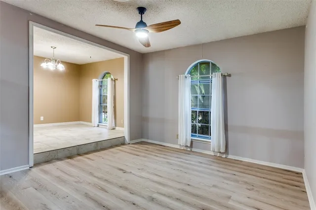 an empty room with wooden floor chandelier fan and windows
