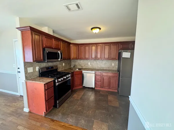 a kitchen with stainless steel appliances granite countertop a stove top oven a sink dishwasher and a refrigerator with wooden cabinets
