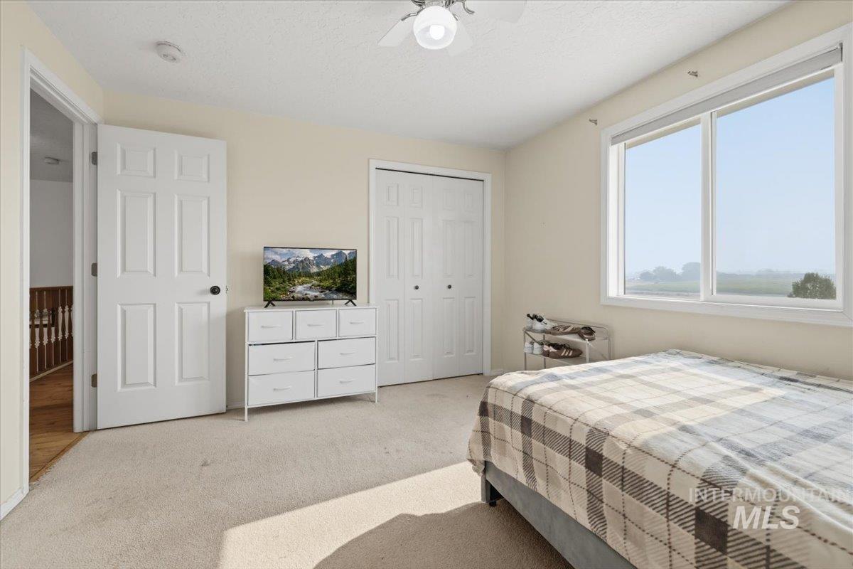 24440 Kenridge Road Caldwell, ID 83607 - Photo 36 of 48 Bright room with a large window overlooking a distant field, featuring light-colored carpeting, a ceiling fan with integrated lighting, and a white bi-fold closet door
