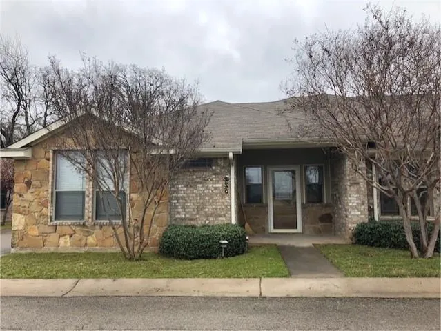a view of a brick house with a yard plants next to a road