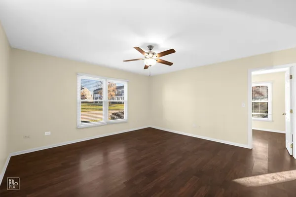 a view of an empty room with wooden floor and a ceiling fan