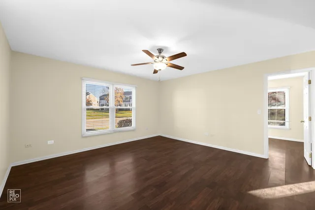 a view of an empty room with wooden floor and a ceiling fan
