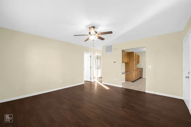 a view of an empty room with wooden floor and a ceiling fan