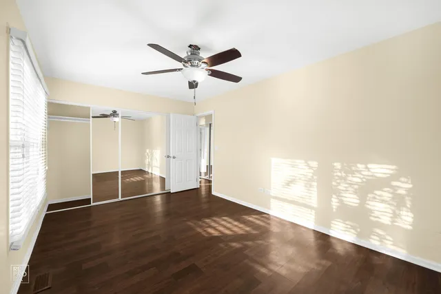an empty room with wooden floor fan and windows