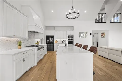 a large white kitchen with stainless steel appliances granite countertop a stove oven a white countertops with cabinets and wooden floor