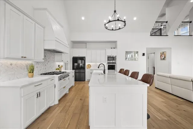 a large white kitchen with stainless steel appliances granite countertop a stove oven a white countertops with cabinets and wooden floor