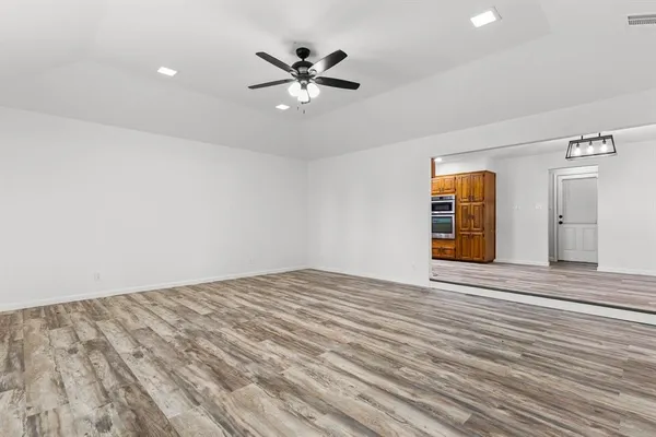 an empty room with wooden floor fan and windows