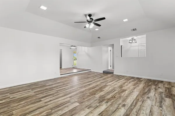 an empty room with wooden floor ceiling fan and windows