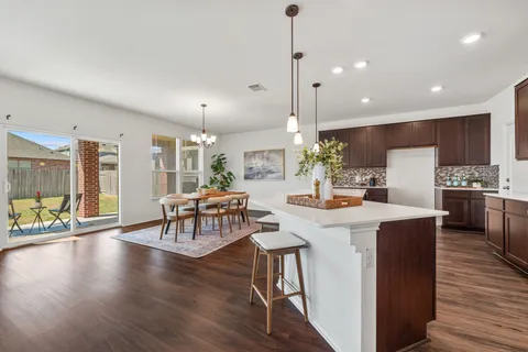 a kitchen with stainless steel appliances kitchen island granite countertop a stove a refrigerator a kitchen island a dining table and chairs with wooden floor