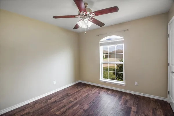 an empty room with wooden floor chandelier fan and windows