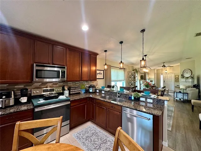 a kitchen with stainless steel appliances granite countertop a refrigerator a stove a sink dishwasher a dining table and chairs with wooden floor