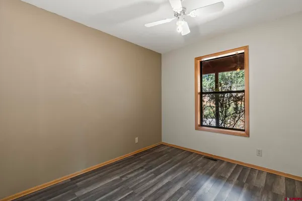 an empty room with wooden floor chandelier fan and windows